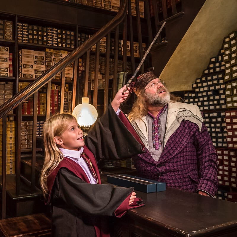 Un integrante del equipo en Ollivanders le ayuda a una niña elegir la varita mágica perfecta en esta tienda de Diagon Alley, en The Wizarding World of Harry Potter de Universal Studios Orlando.