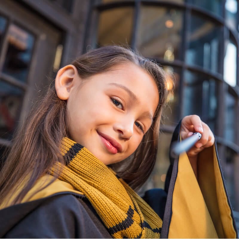 Una niña Hufflepuff™ sonrie mientras apunta su varita mágica en The Wizarding World of Harry Potter™.