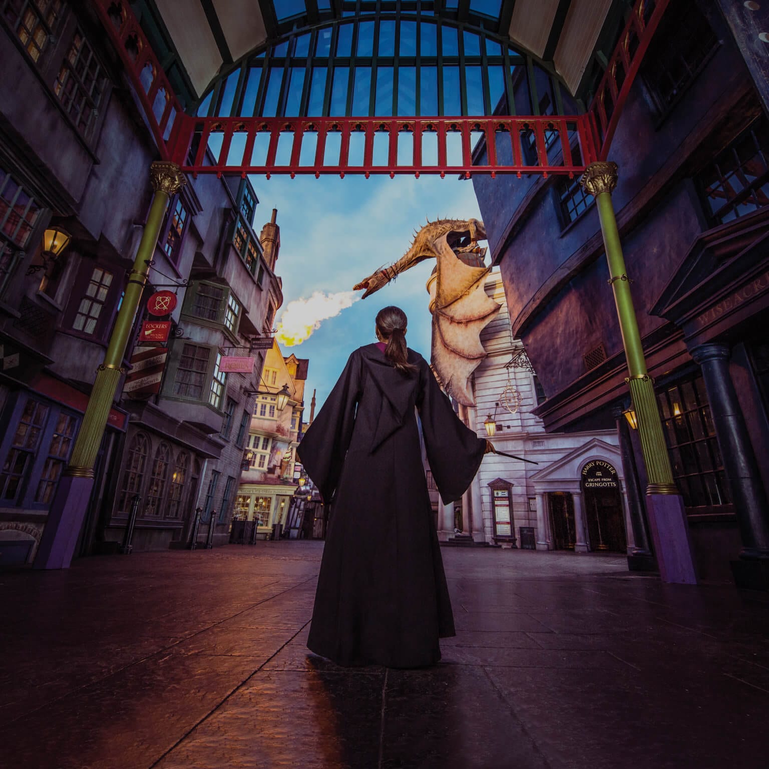 Una niña con una túnica de mago parada en The Wizarding World of Harry Potter Diagon Alley™ mientras un dragón lanza fuego.