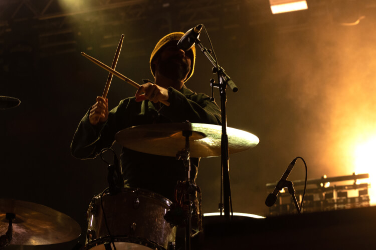 A drummer is silhouetted against the bright lights of a concert stage.&nbsp;