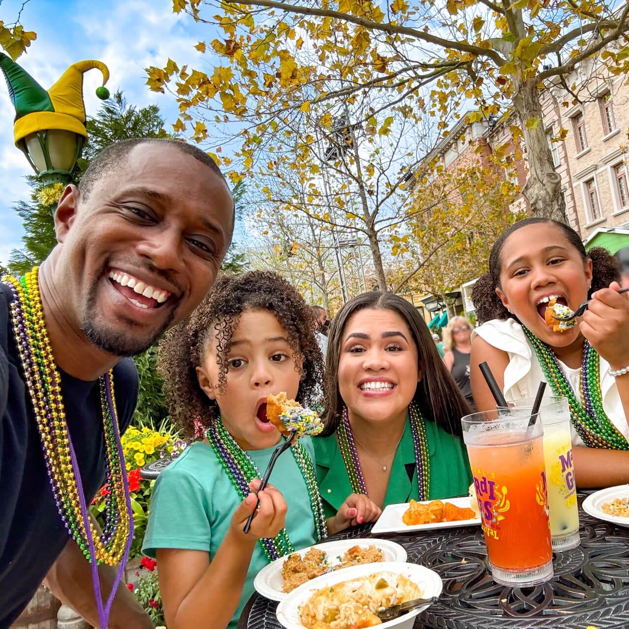 Una familia con coloridos collares de Mardi Gras y disfrutando de la comida durante el Universal Mardi Gras.