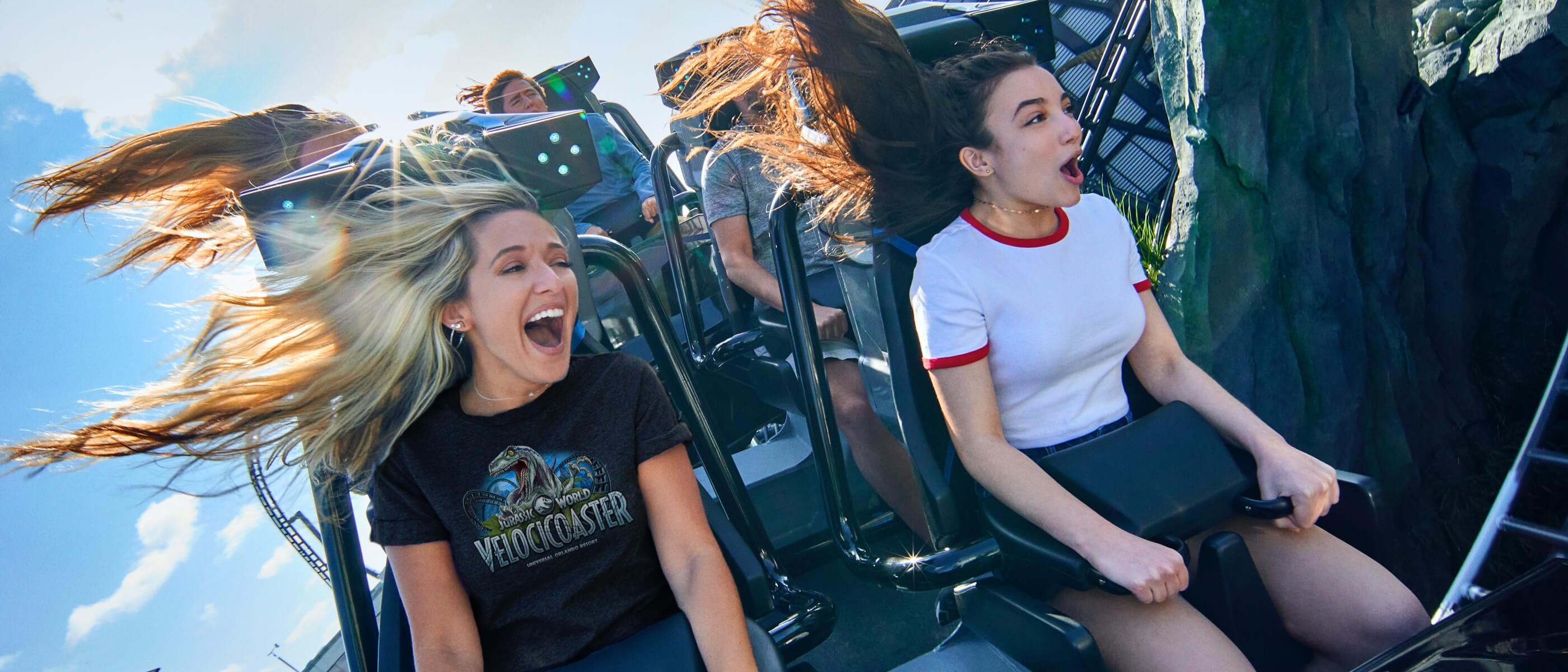 Dos mujeres gritando de emoción en una montaña rusa con el viento que despeina sus cabellos.