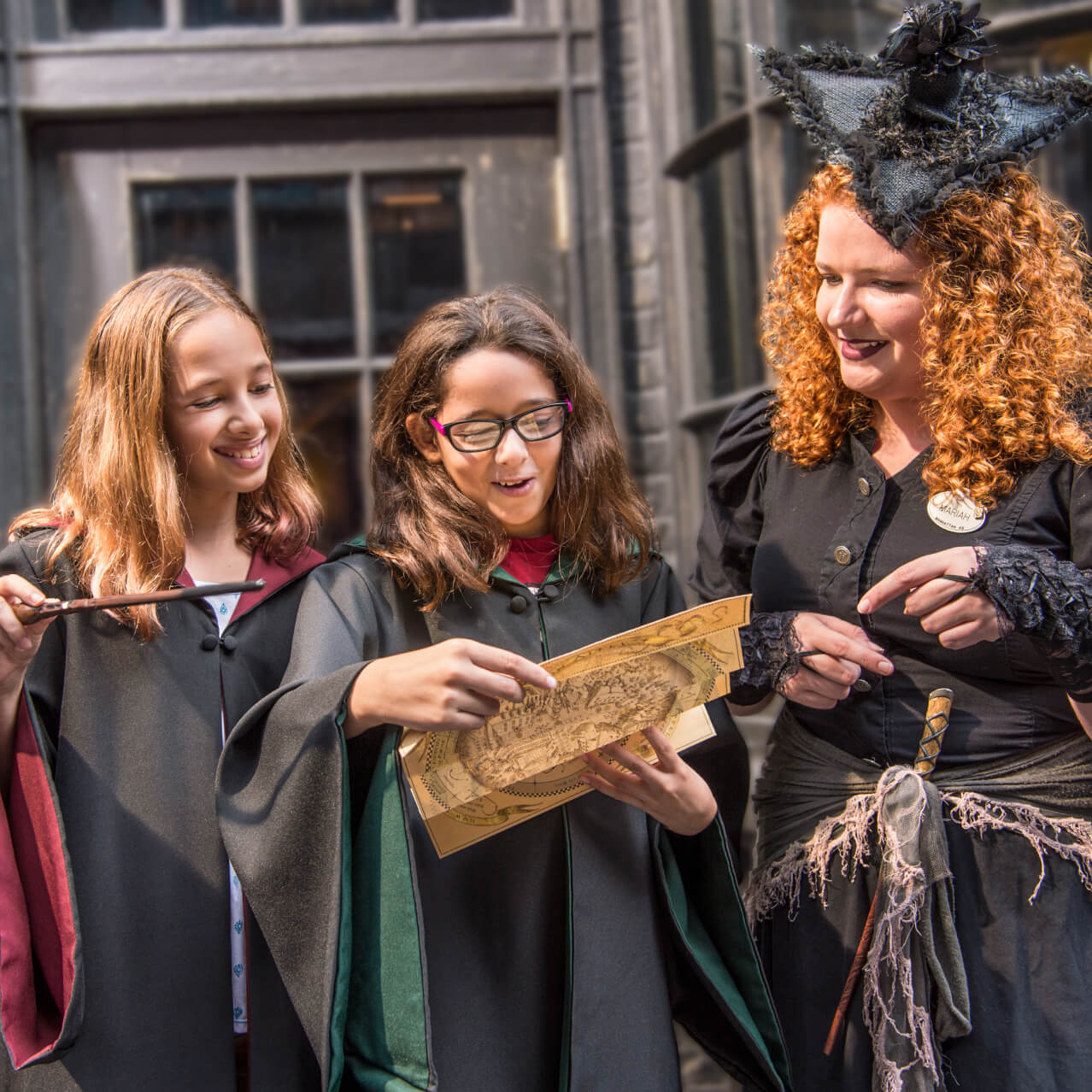 Smiling friends with wizarding robes and wands examining a map with the help of a Team Member in a black witch’s gown.