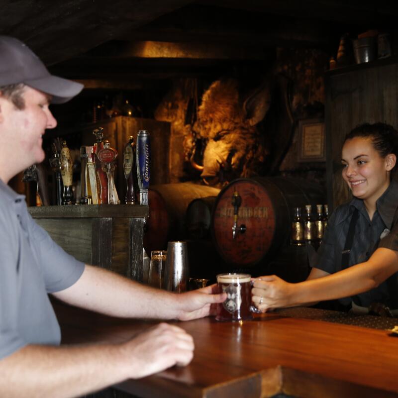 Una mujer sonríe y entrega una cerveza a un cliente con un bar detrás de ella.