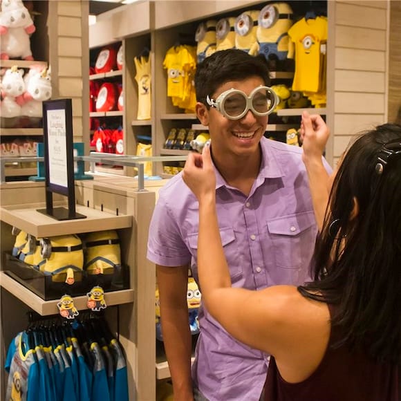 Una mujer coloca gafas de Minions sobre el rostro de su esposo dentro del Universal Studios Store en Loews Sapphire Falls Resort at Universal Orlando.
