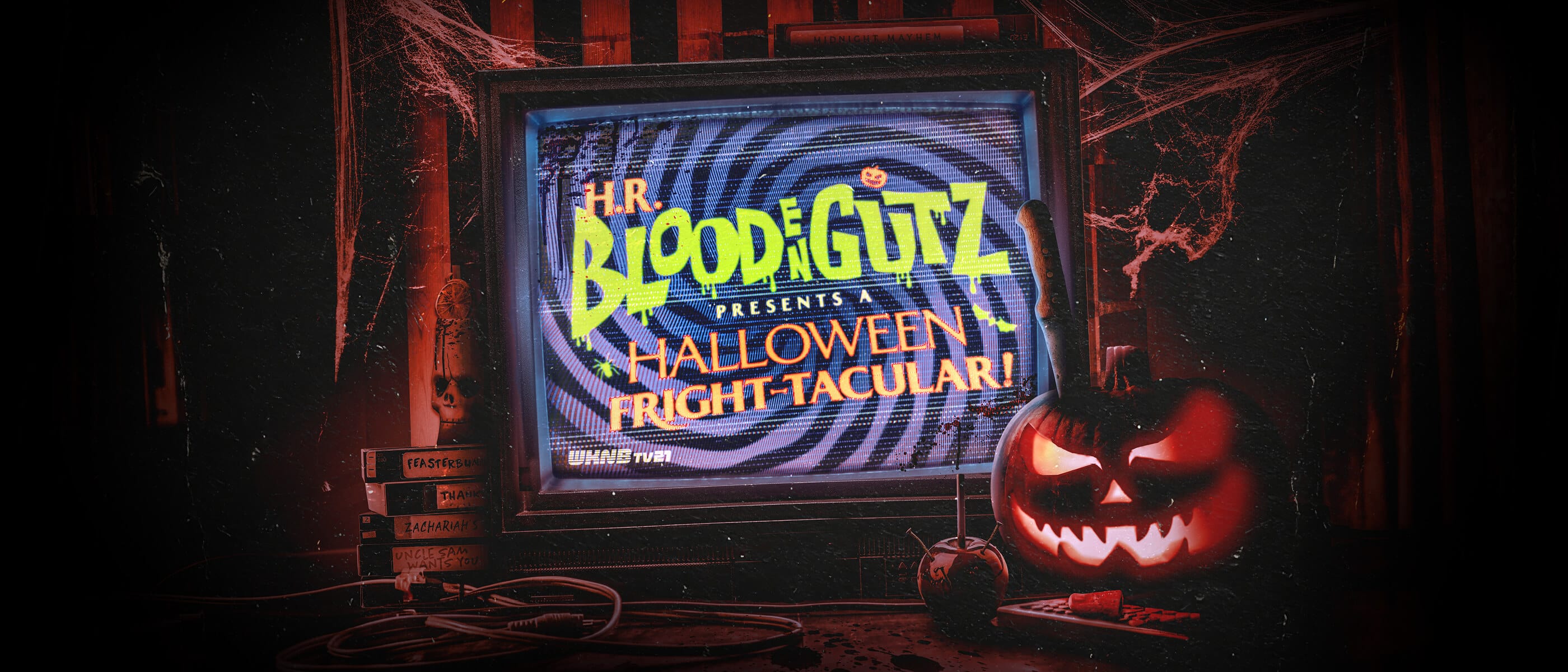 Las palabras “H.R. BLOODENGUTZ PRESENTS A HALLOWEEN FRIGHT-TACULAR!” en un televisor viejo junto a cintas VHS y una linterna de calabaza.