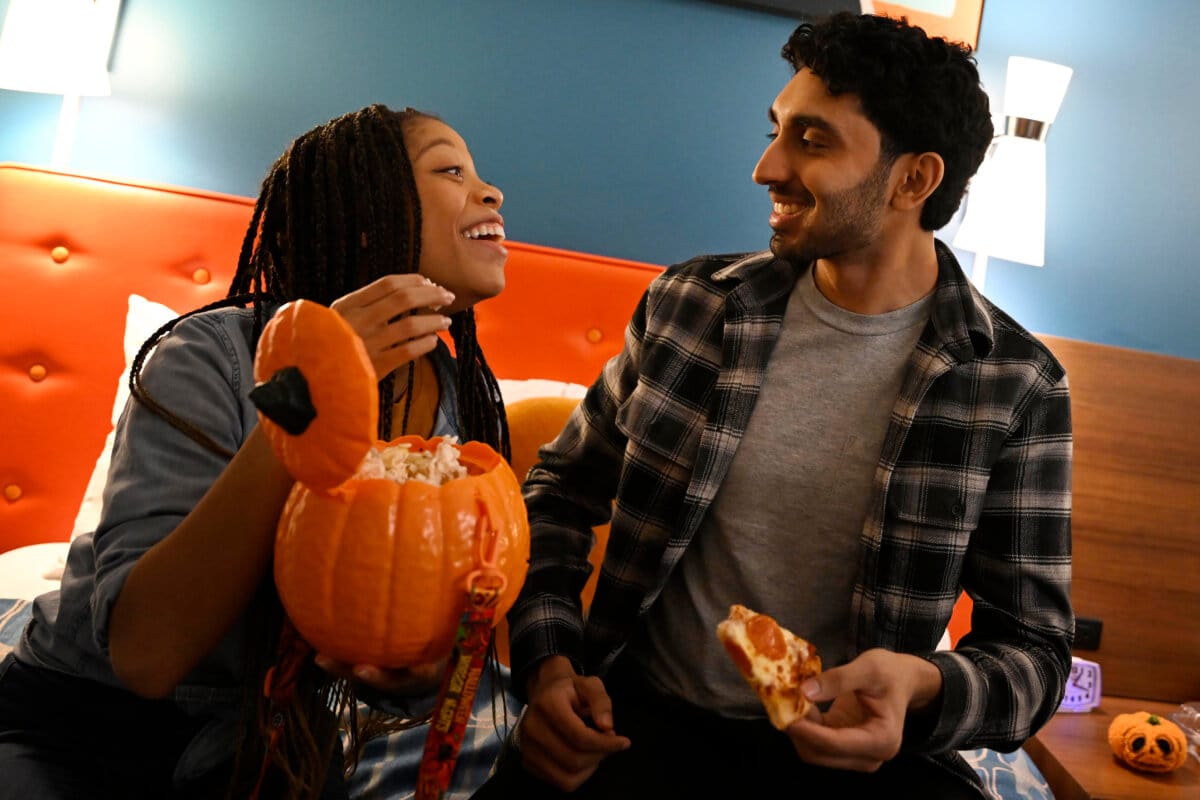 A couple enjoying popcorn from a pumpkin-shaped bucket and a slice of pizza in their Cabana Bay Beach Resort hotel room.