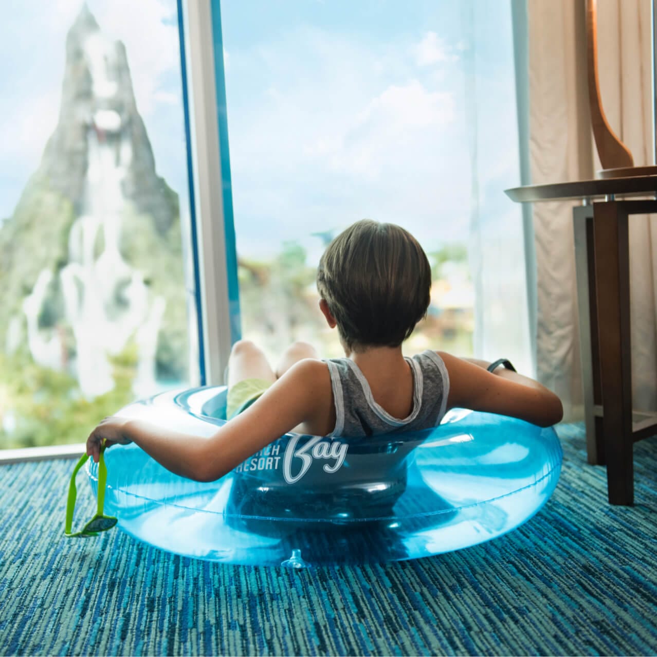 Um garoto olha pela janela de seu quarto de hotel Cabana Bay para ver o Universal© Volcano Bay.
