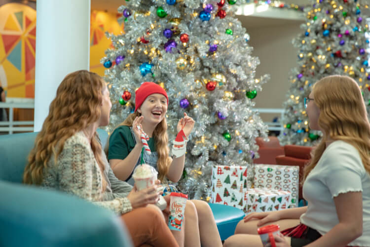 A family of three are sitting near Christmas trees in the lobby of Universal's Cabana Bay Beach Resort.