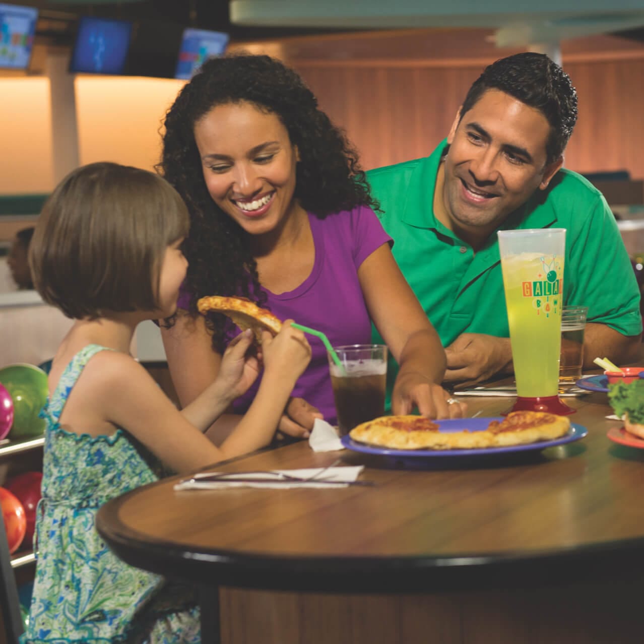 Pais dão risada enquanto a filha come um pedaço de pizza no Galaxy Bowl Restaurant do Universal's Cabana Bay Beach Resort.