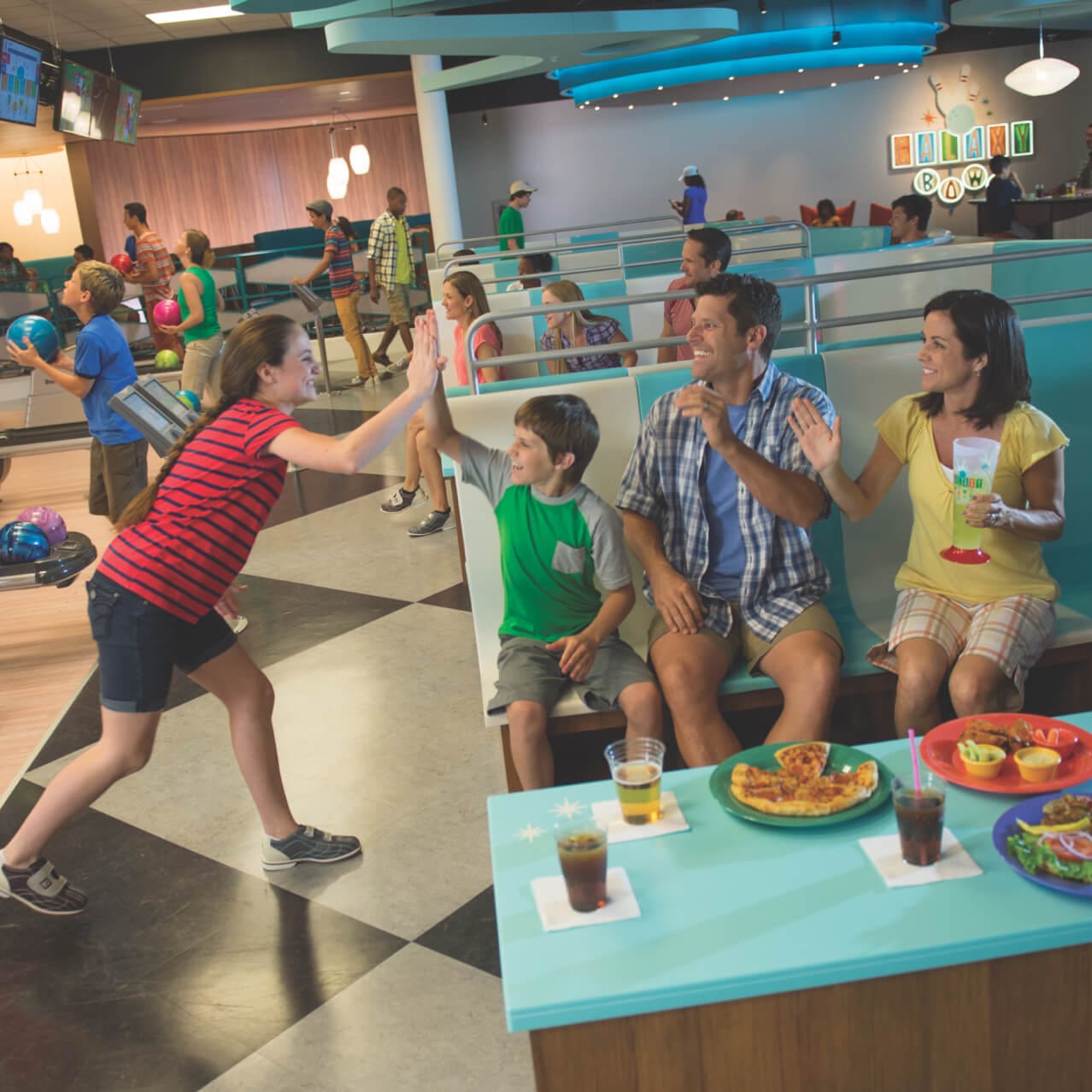 Um irmão e uma irmã batem as palmas das mãos enquanto seus pais dão risada no Galaxy Bowl, no Universal’s Cabana Bay Beach Resort.