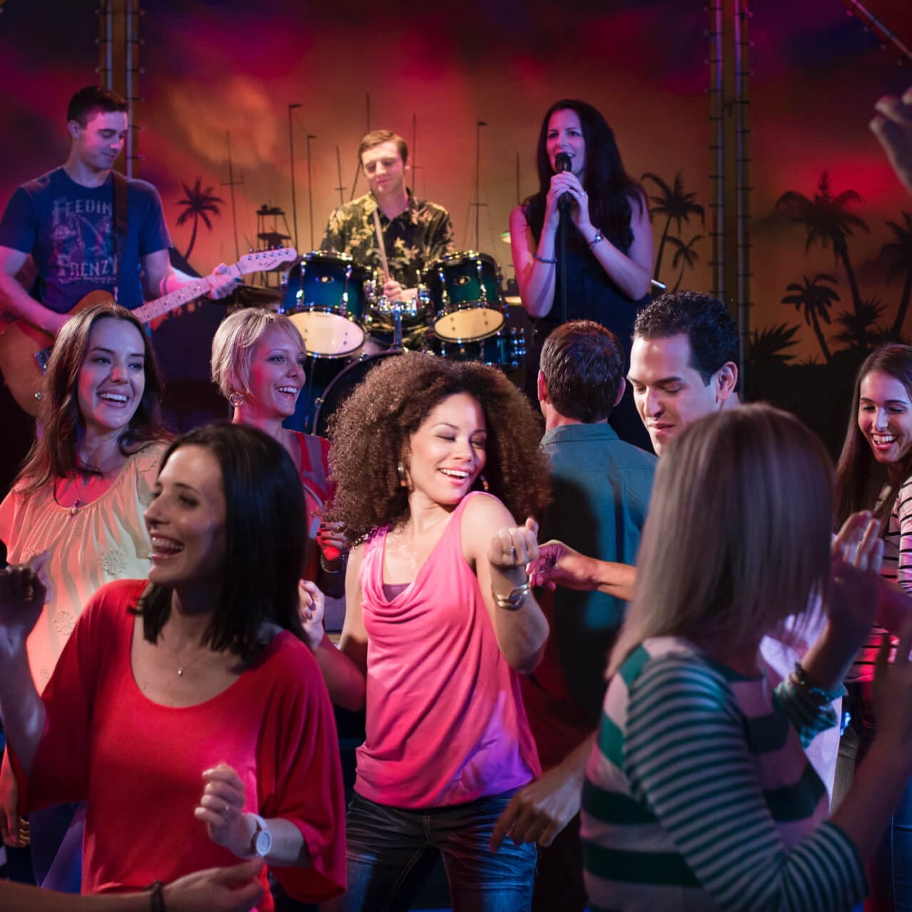 Clientes dançam enquanto um cantor, um guitarrista e um baterista tocam ao vivo no palco do Jimmy Buffett's Margaritaville.
