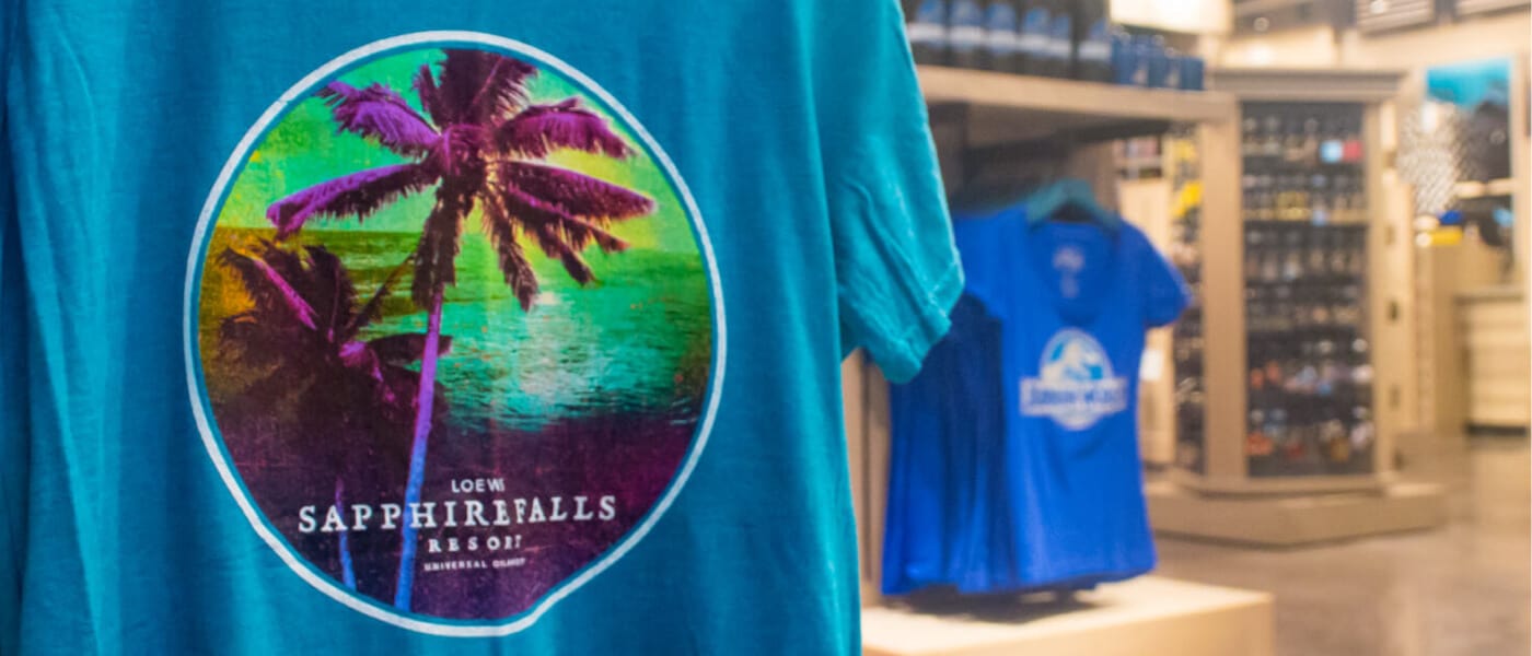 Uma visão de perto de uma camiseta do Loews Sapphire Falls Resort com o Universal Studios Store ao fundo.