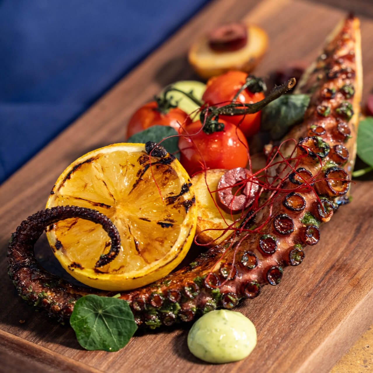 Charred Octopus com batatas crocantes com ervas, azeitonas, salsa verde, folhas brássicas e servido no Bar Helios.