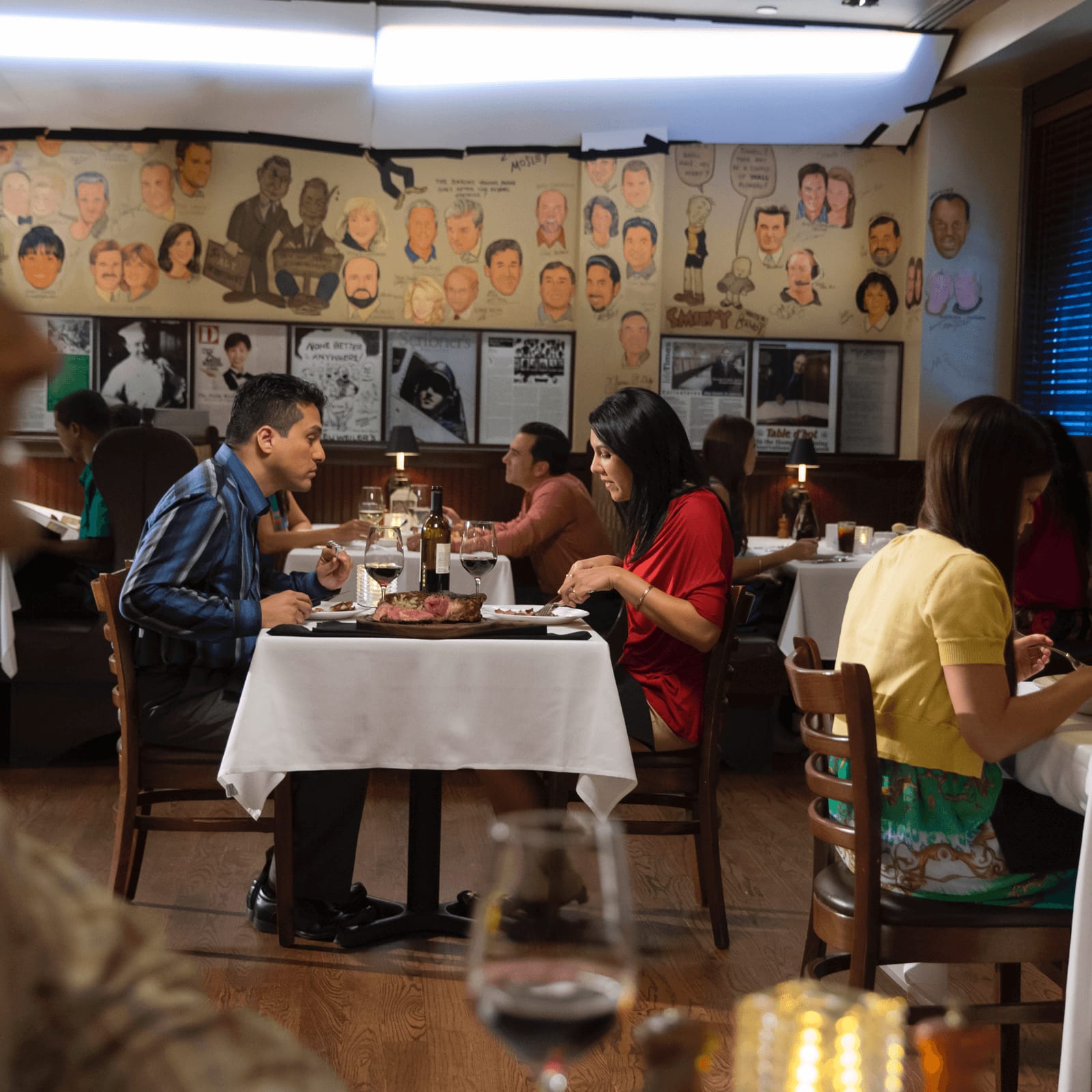 Os visitantes desfrutam de vinho e de uma refeição requintada em uma mesa de jantar adornada com toalhas brancas no restaurante do Hard Rock Hotel, The Palm.