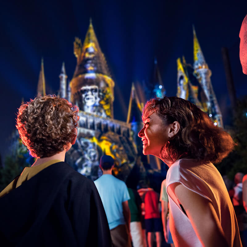 Um irmão e uma irmã estão animados enquanto experimentam o show Dark Arts at Hogwarts™ Castle.