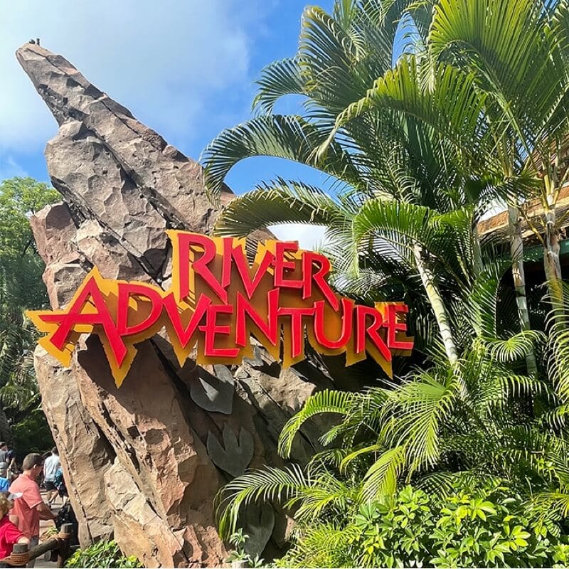 Placa da River Adventure em vermelho e amarelo em uma rocha gigante cercada por folhagem.