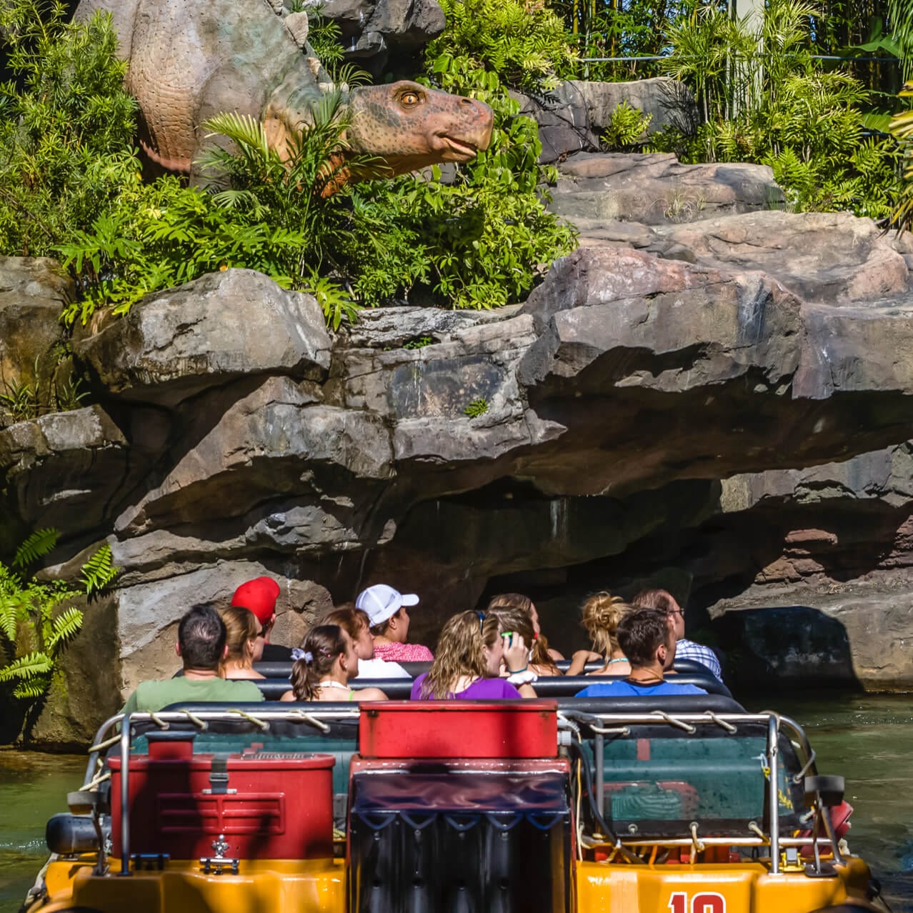 Vista de trás dos visitantes do parque temático flutuando ao longo da água durante parte da experiência da atração Jurassic Park River Adventure no Universal Orlando.
