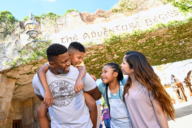 Uma família feliz de quatro pessoas em frente ao letreiro “The adventure begins” no Port of Entry dentro do Universal Islands of Adventure.