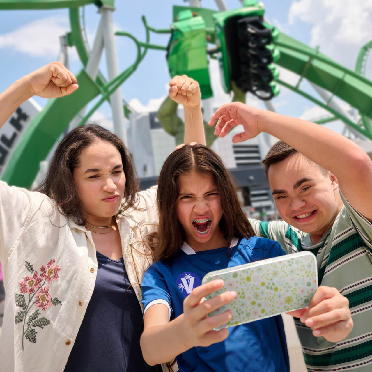 A family of three take a selfie in front of The Incredible Hulk Coaster, raising their arms and making their best Hulk impressions.