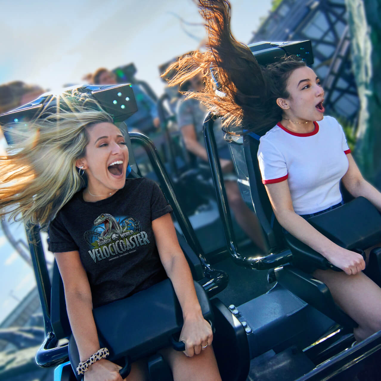 Two girls scream and smile as they grip the handles on the VelociCoaster ride at Universal Islands of Adventure.
