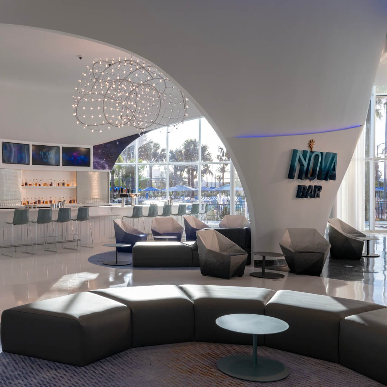 O Nova Bar, um espaçoso e futurista bar do lobby interno do Universal Stella Nova Resort, com paredes fluidas e janelas panorâmicas com vista para a piscina do lado de fora.