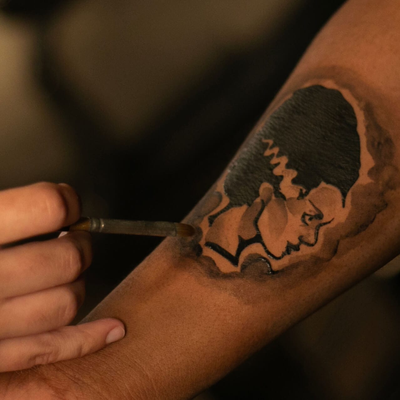 An artist at the Darkmoor Monster Makeup Experience applying a Bride of Frankenstein temporary tattoo to a customer's arm.