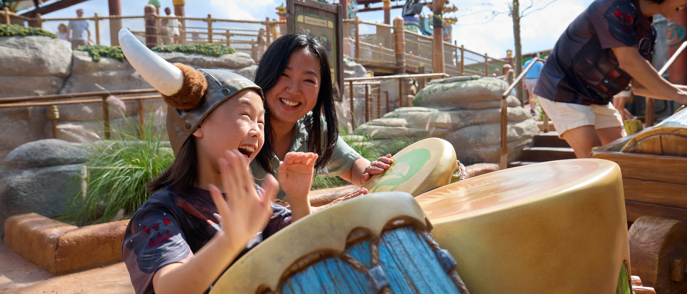 Uma jovem e uma mulher riem e tocam bateria no Viking Training Camp do How to Train Your Dragon - Isle of Berk, no Universal Epic Universe.