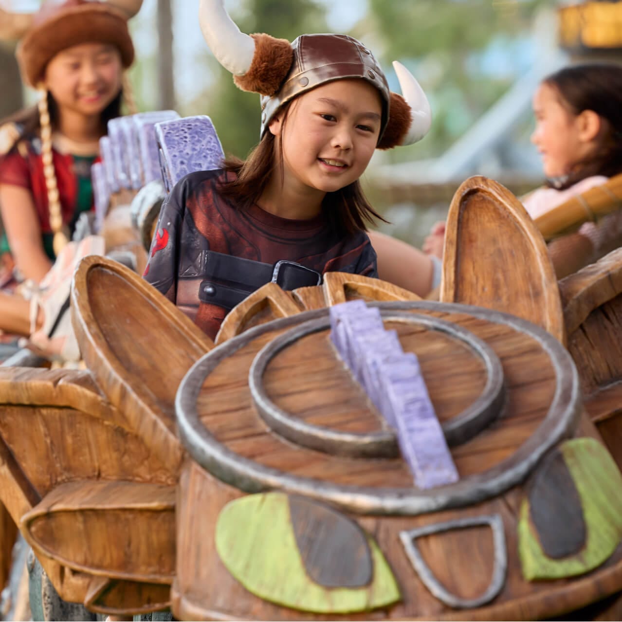 Jovens visitantes usando capacetes viking brincam no playground temático de dragão no Viking Training Camp de How to Train Your Dragon - Isle of Berk.