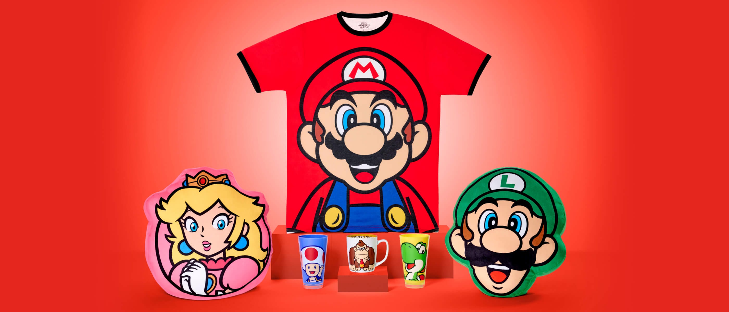 Produtos dos personagens da Nintendo™, incluindo uma camiseta do Mario, almofadas da Princesa Peach e Luigi, copos do Toad e Yoshi, e uma caneca do Donkey Kong, do SUPER NINTENDO WORLD™