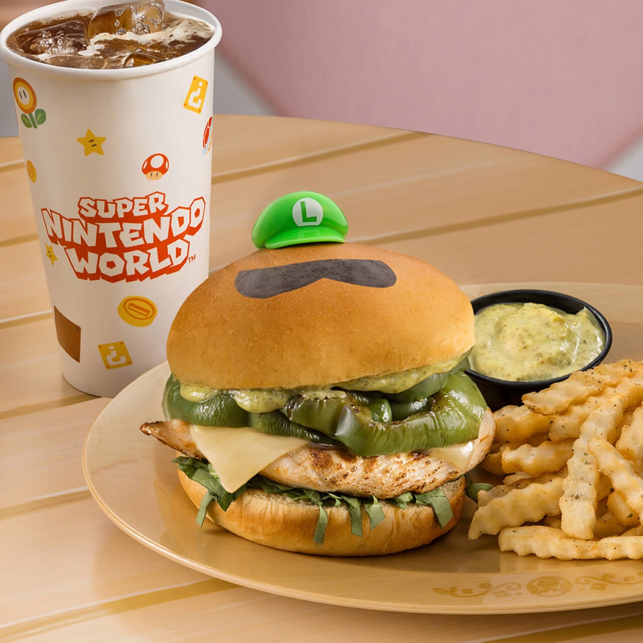 Um Luigi Burger de frango grelhado coberto com pesto de manjericão, queijo suíço derretido, pimentões verdes e espinafre fresco, em um pão de brioche com batatas fritas trufadas, disponível no Toadstool Cafe.