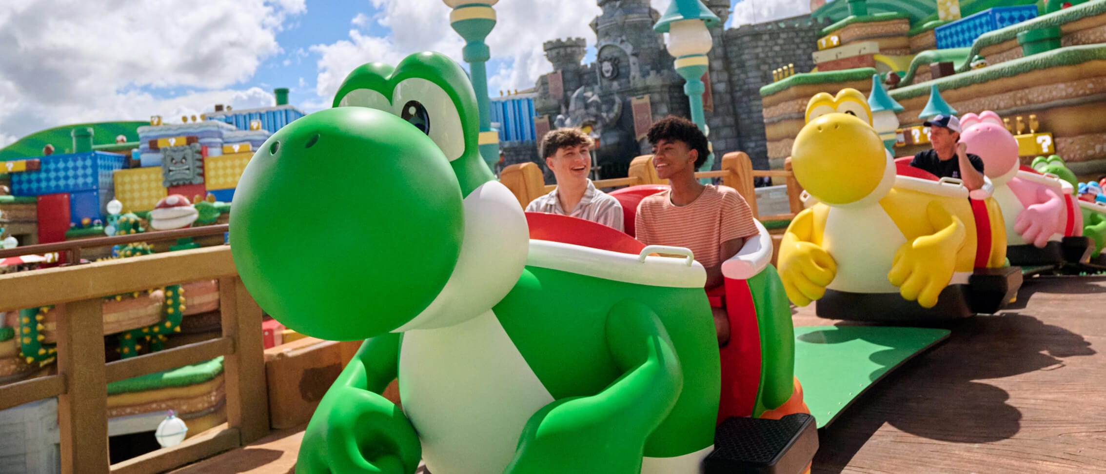 Smiling Guests in different-colored Yoshi vehicles with a castle and colorful buildings in view.
