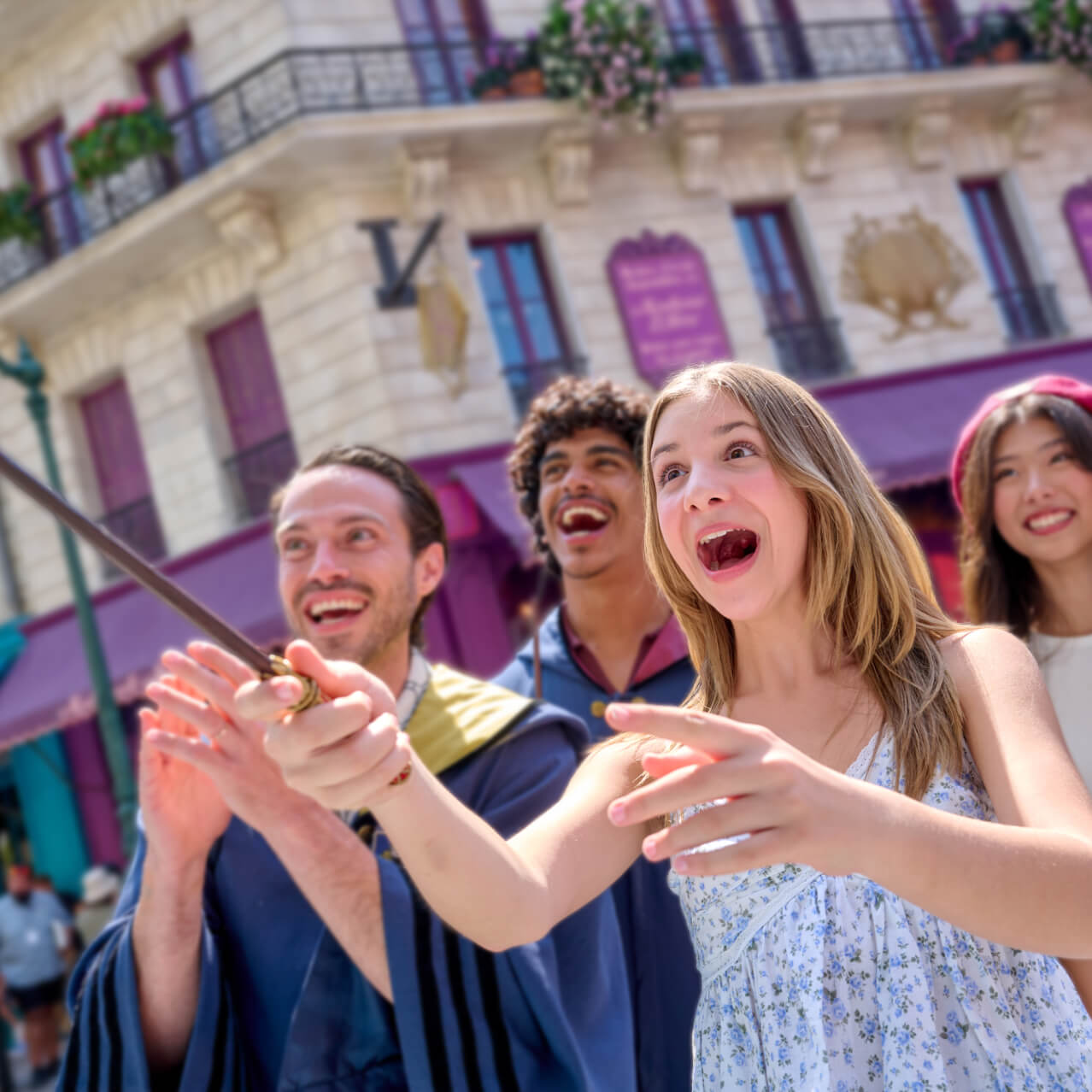 Smiling friends in wizarding gear looking on as an excited Guest points a wand on the colorful Paris streets.