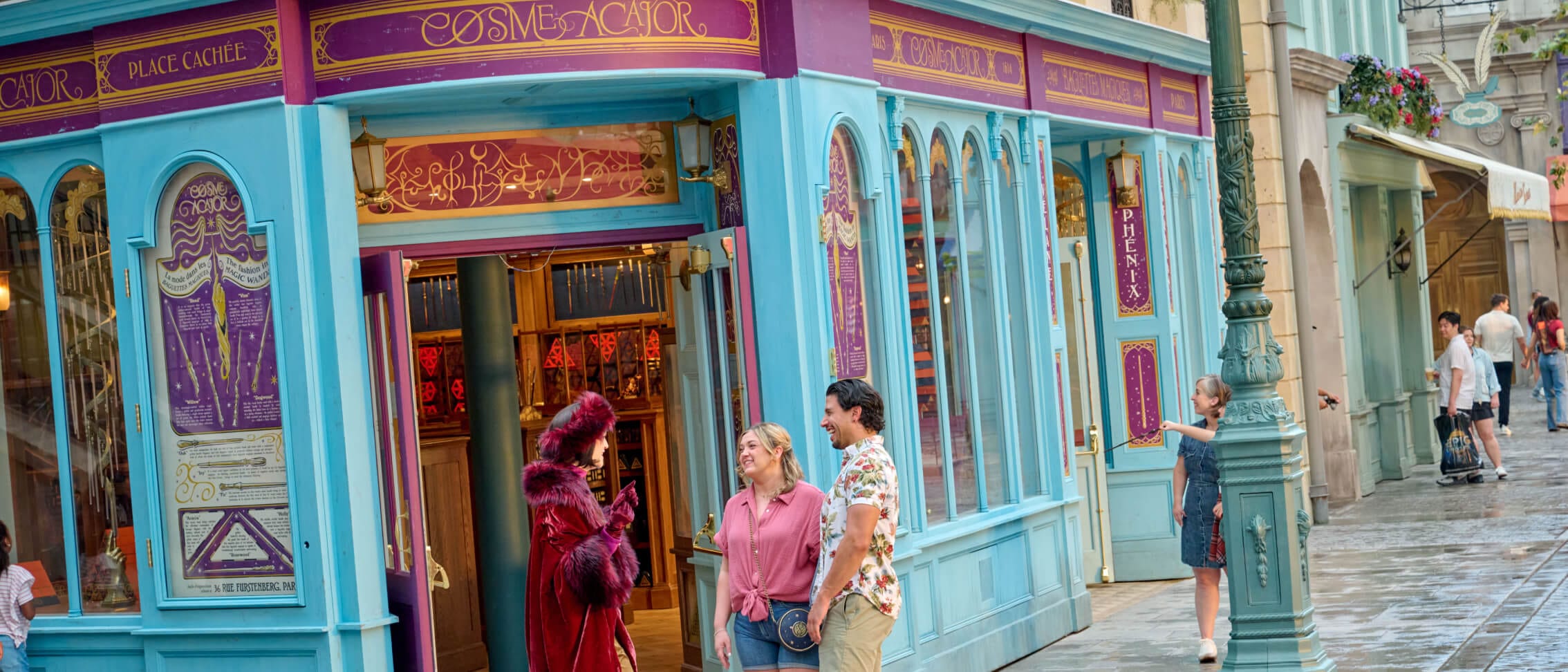 A couple is greeted by the esteemed wandmaker Cosme at the entrance of Cosme Acajor Baguettes Magiques.