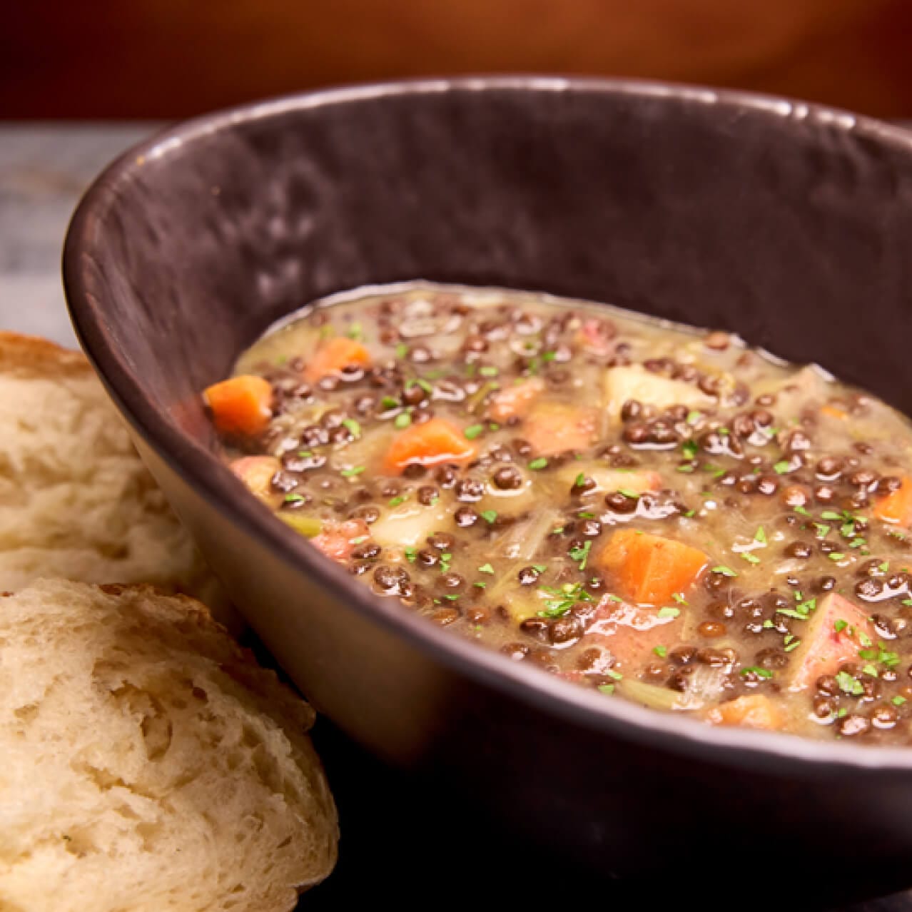 Lentil Stew, uma mistura de lentilhas macias, bacon vegano saboroso e raízes vegetais frescas. Servido com pão artesanal no Le Gobelet Noir.
