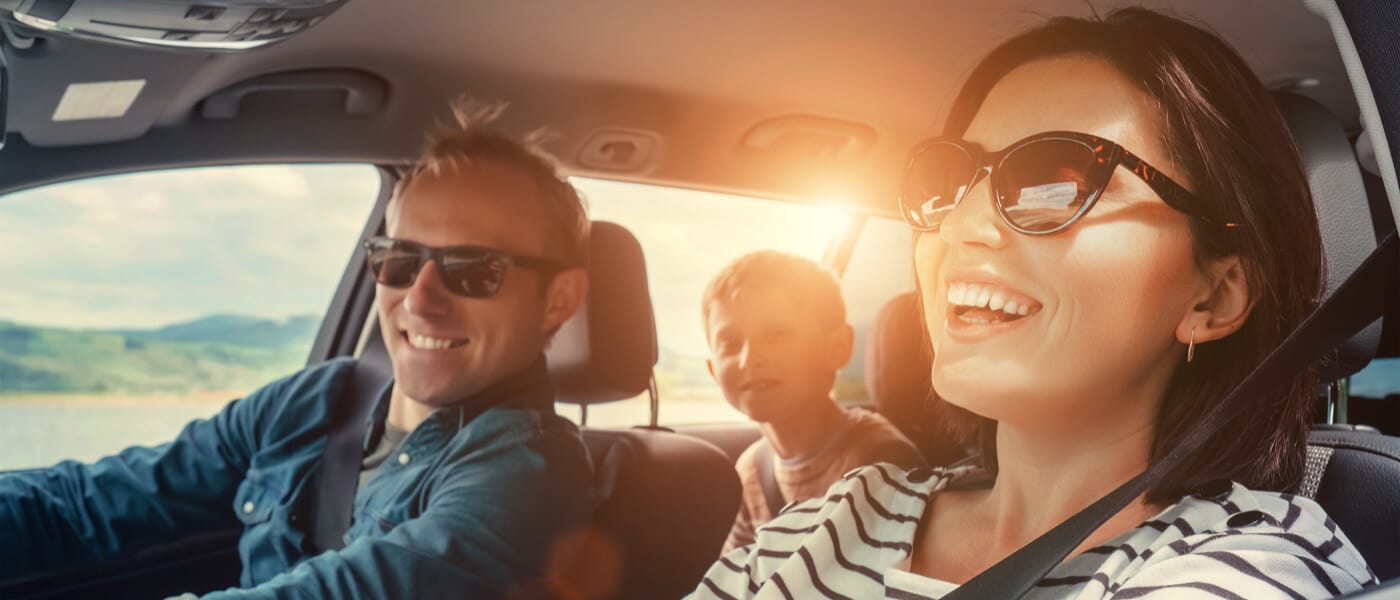 Pai, mãe e filho sorrindo dentro do carro.