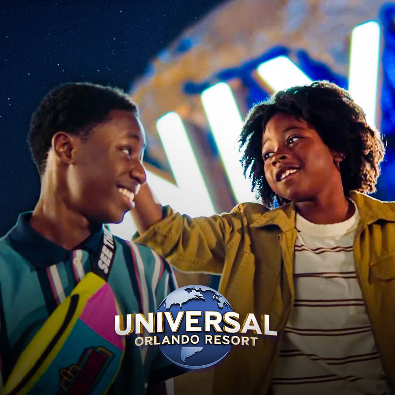 A young Guest and his older brother smiling at each other as the iconic Universal globe glows behind them.