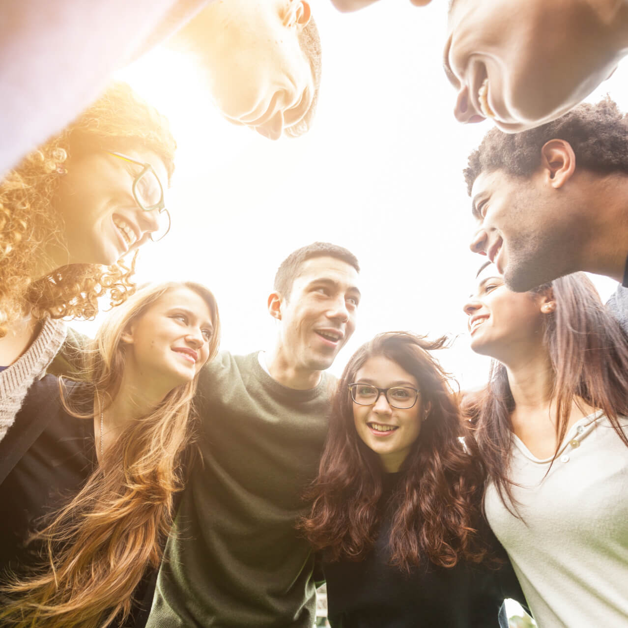 A group of young people huddle together while smiling at each other.