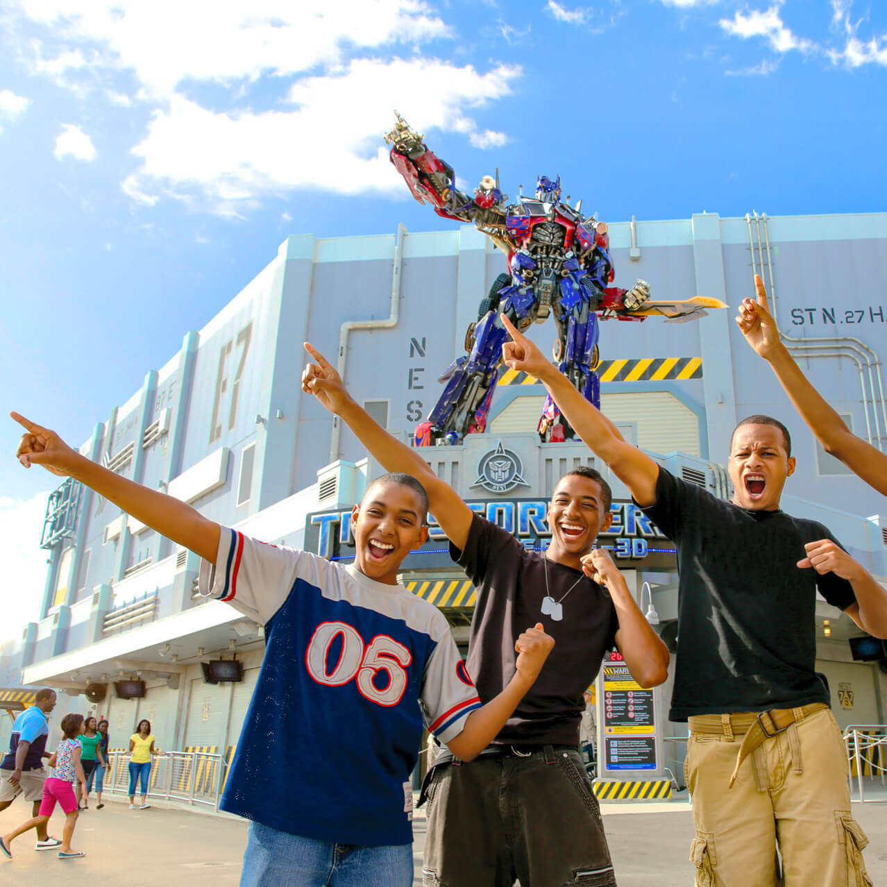Guests point towards the sky, mimicking the pose of Optimus Prime, who stands atop the entrance to TRANSFORMERS: The Ride 3D at Universal Studios Orlando.