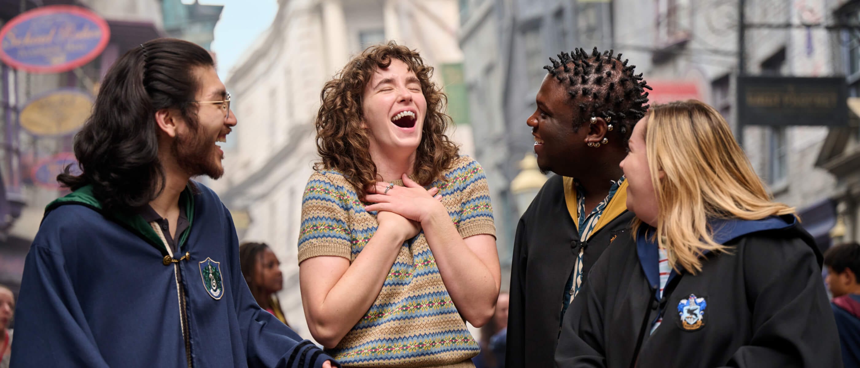 A Guest laughing with joy surrounded by friends in wizarding robes with Diagon Alley™ and Gringotts™ Bank in the background.