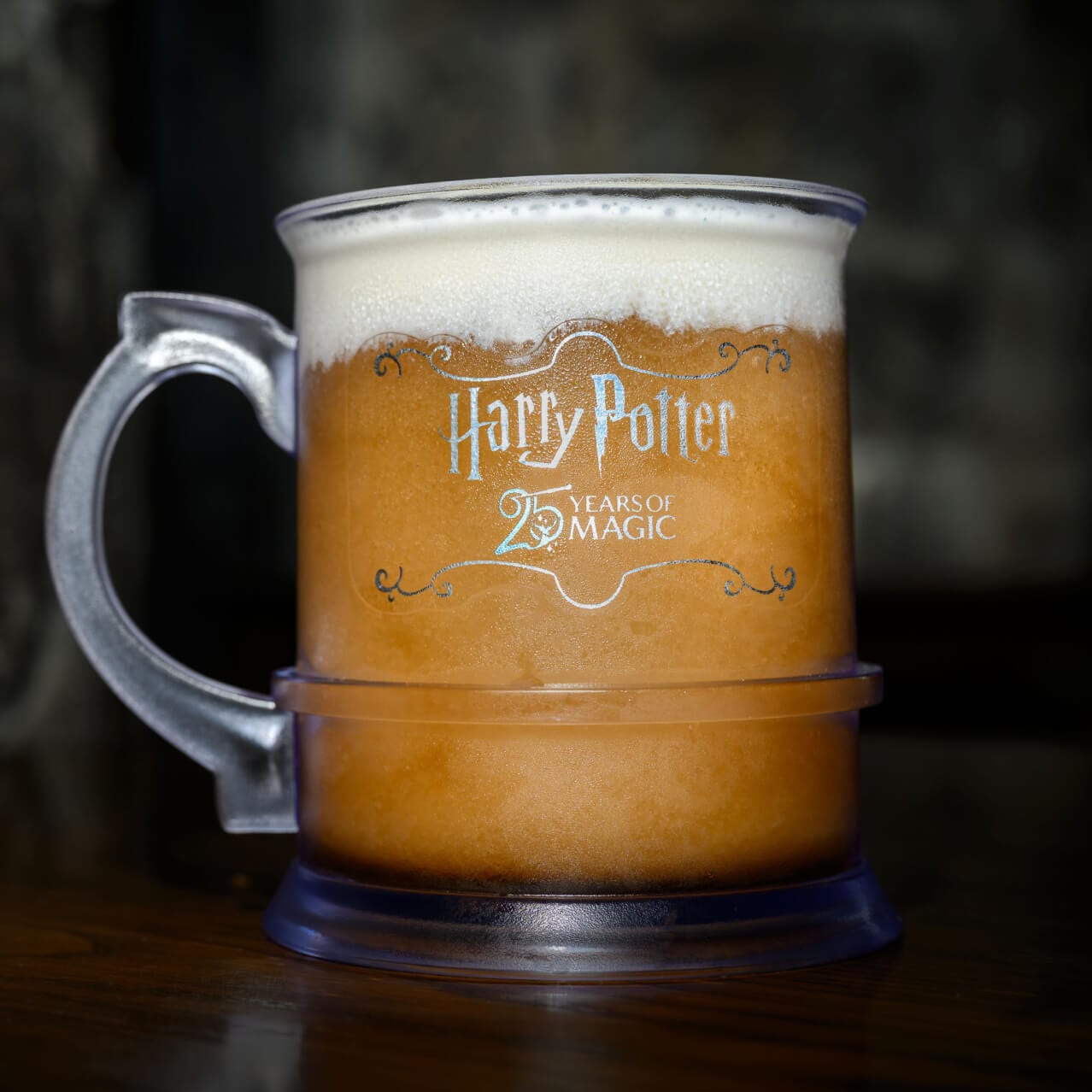 A mug of sudsy Butterbeer with the words ‘Harry Potter 25 Years of Magic’ on the side, sitting on a dark wood table.