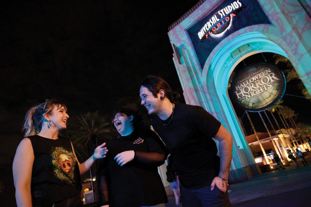 Friends laughing in front of the eerily lit Universal Studios Florida entry arch with a Halloween Horror Nights sign.