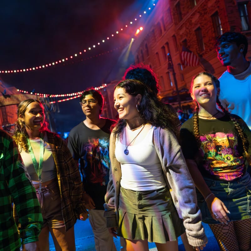 A group of unsuspecting friends smiling as they walk along the night streets, unaware of any scareactors lurking nearby.