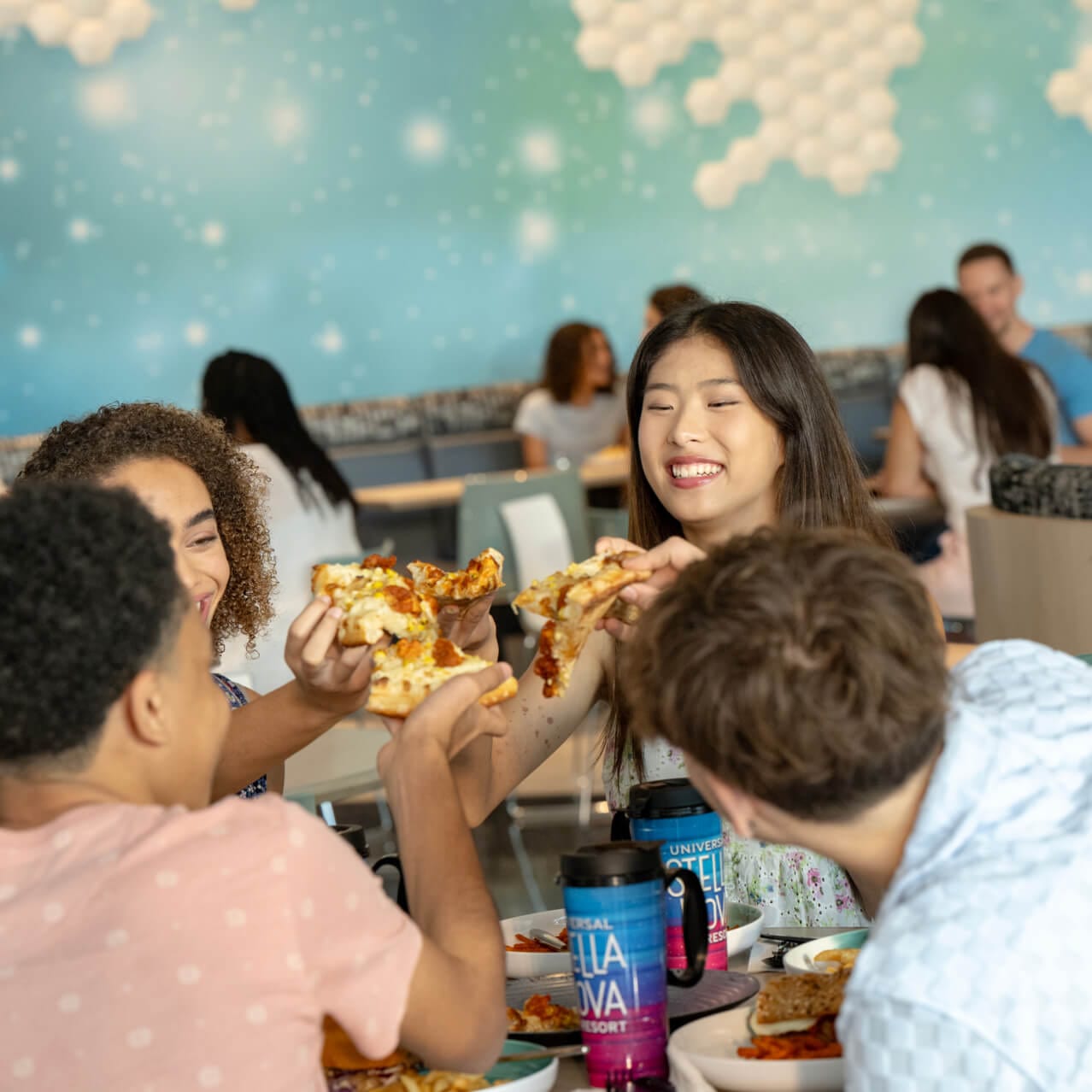 Five friends enjoying food and drinks inside of the Cosmos Cafe and Market at Universal Stella Nova Resort.