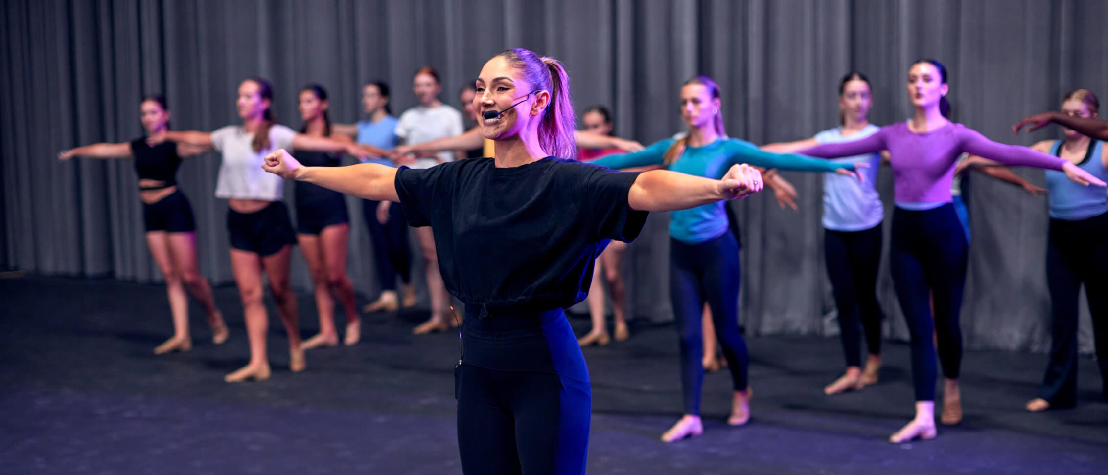 Youth dancer performing on stage in black leotard.