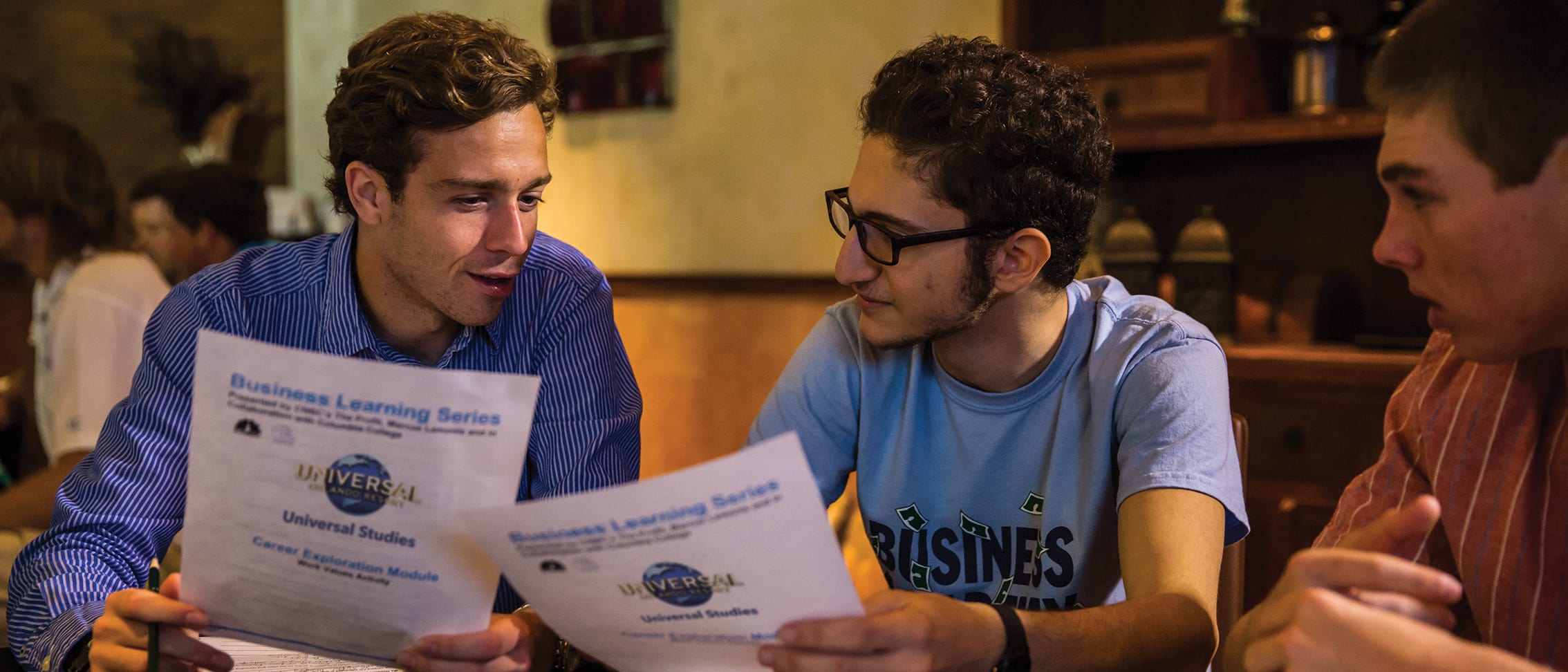Students holding papers that have the Universal Orlando Resort logo and the words Business Learning Series on them