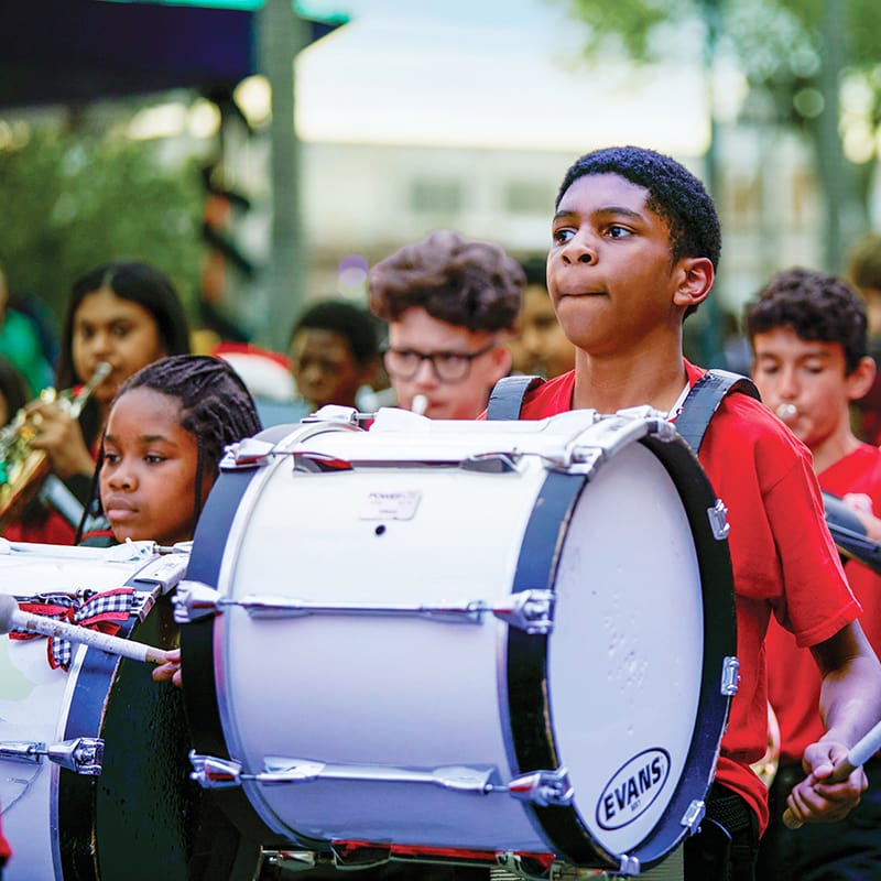 A young man plays the bass drum in a marching band parading through Universal Studios Florida.