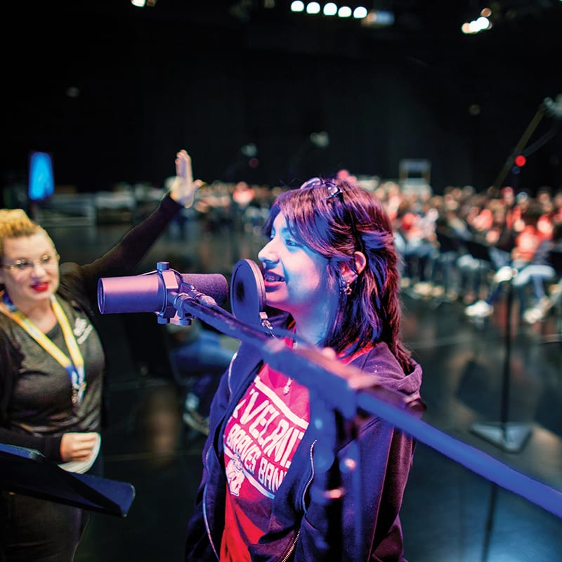 A young woman takes a vocal solo with a choir behind her at a youth program workshop in Universal Studios Orlando.