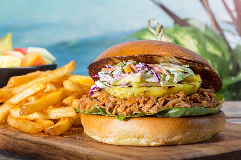 A Mango BBQ Pulled Pork Sandwich topped with caramelized pineapple and fresh cabbage and mango slaw on a toasted King’s Hawaiian roll sits next to a plate of delicious fries at Volcano Bay.