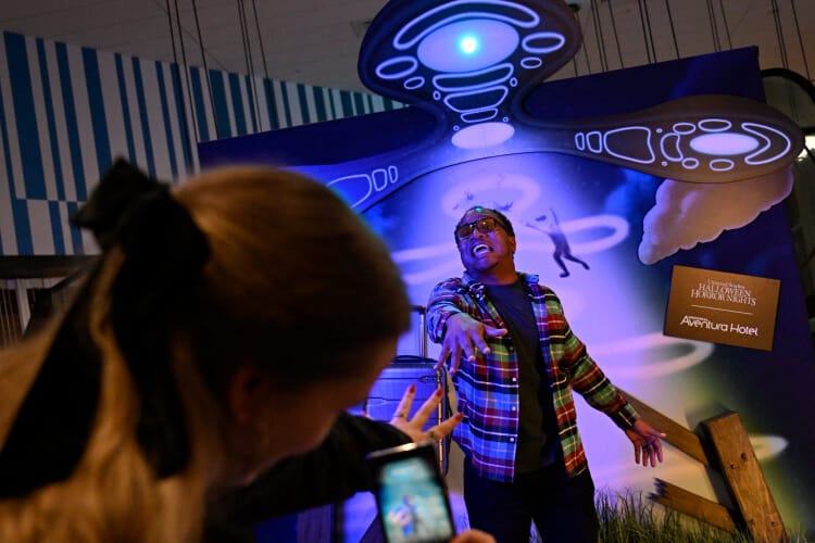 Guests pose with hands outstretched toward each other in front of a phone-activated alien abduction-themed backdrop in the Aventura Hotel lobby.